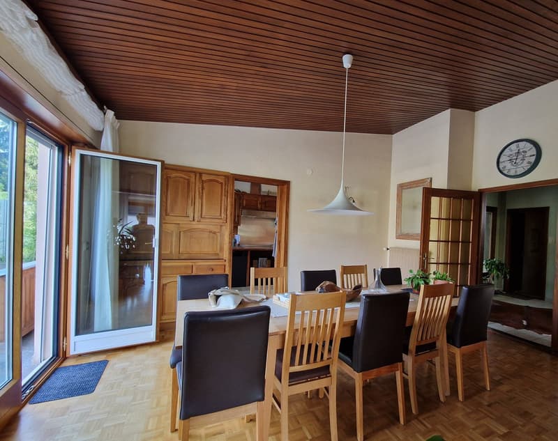 Wooden ceiling, large windows, wooden dining table with 6 chairs, wooden cabinets, clock on the wall