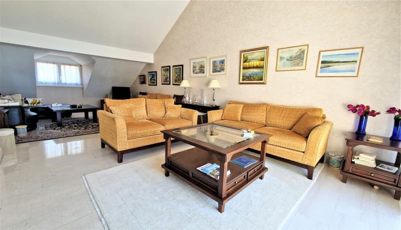 Spacious living room with high ceilings, hardwood floors, and large windows. The room features a set of comfortable yellow sofas, a wooden coffee table, and several framed artwork on the walls. There is also a fireplace visible in the room.