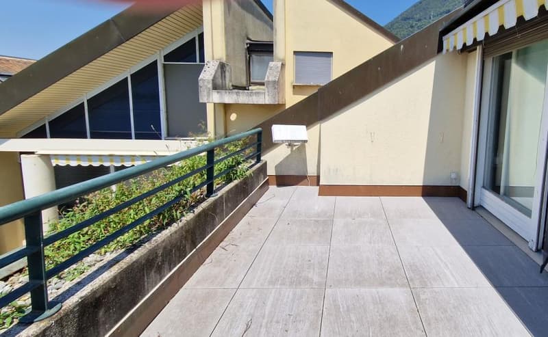 Covered balcony with wooden flooring, metal railing, and a view of the surrounding greenery.