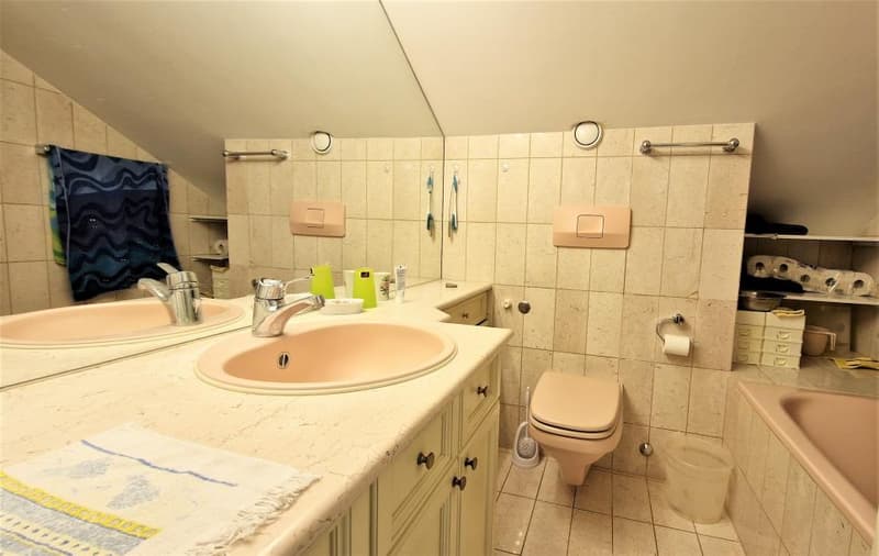Tiled bathroom with a vanity sink, toilet, and storage cabinets. There is a towel and other bathroom items visible.