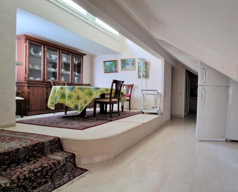 Spacious dining area with a wooden cabinet, dining table and chairs, decorative artwork on the walls, and a tiled floor. A dishwasher is visible in the background.