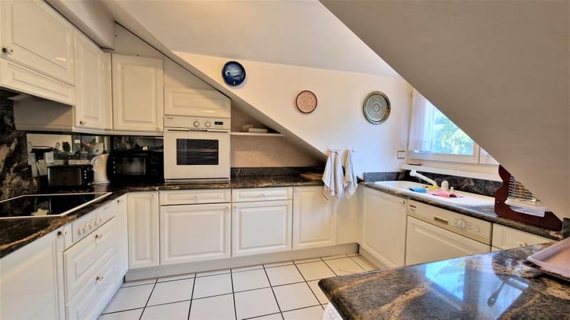 Spacious kitchen with white cabinets, granite countertops, tile flooring, and built-in appliances including a dishwasher