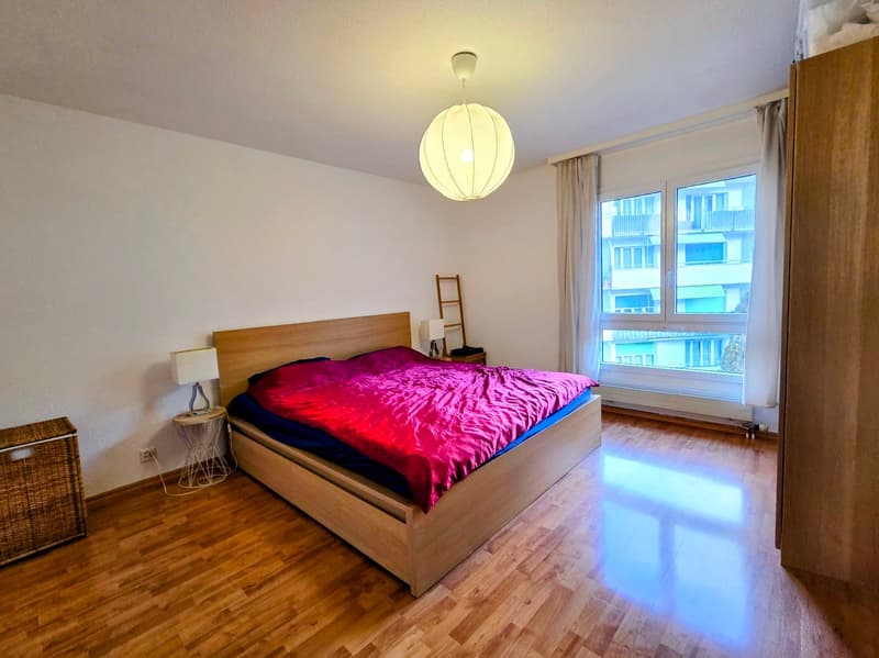 wooden floor, large bed, wooden headboard, nightstands, lamps, windows, curtains, white walls, pendant light