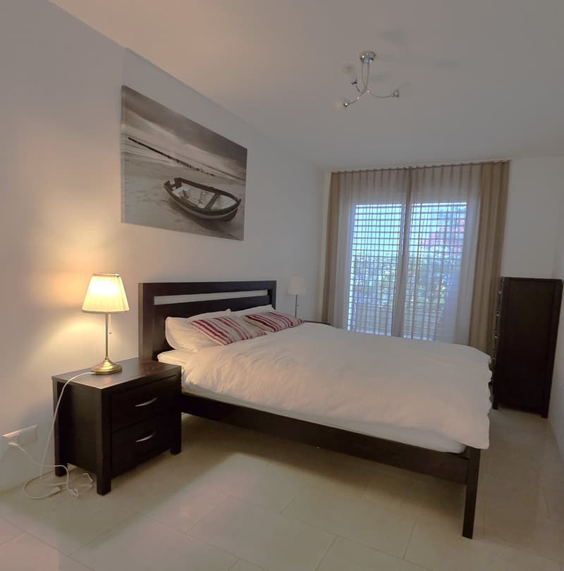 King size bed, white bedding, two nightstands, a wall-mounted picture, a table lamp, a window with curtains, and a closet on the right side of the bed.