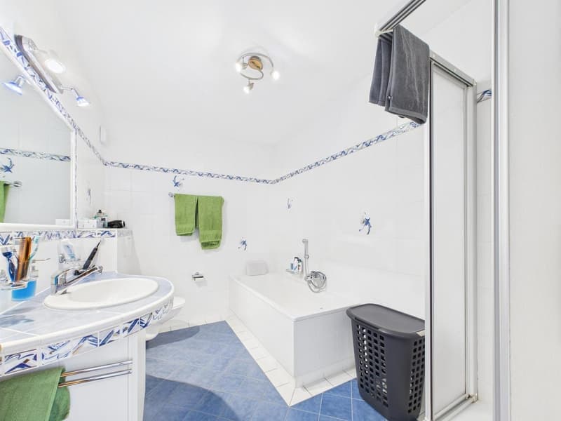 white walls, blue tiled floor, large mirror, double sink, shower enclosure, bathtub, towel rack, and green towels