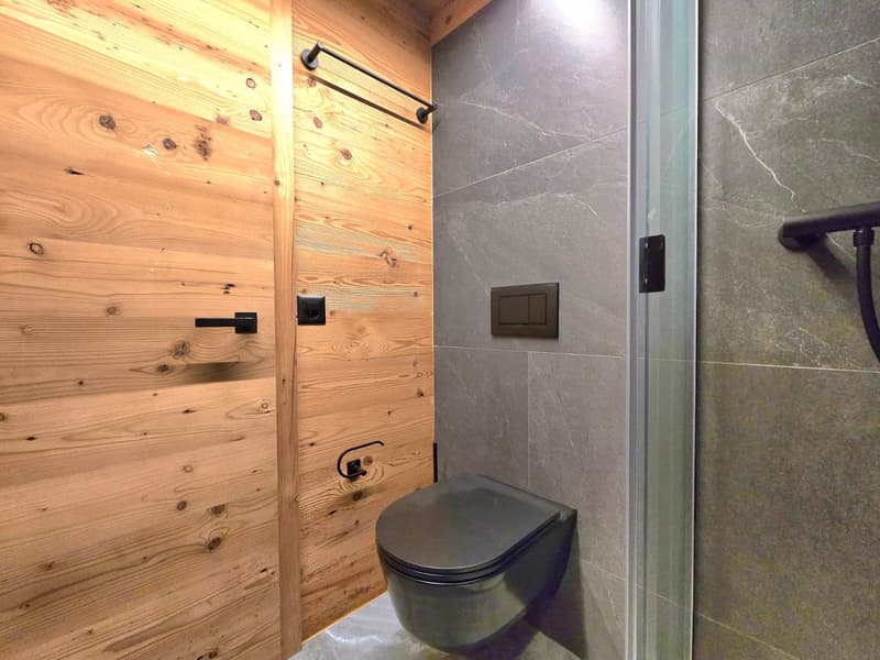 wooden wall, black toilet, glass shower, gray tiles, black handles