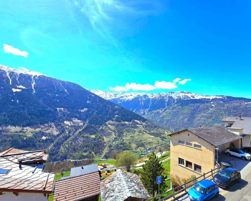 House with mountain view, 3 cars parked in front, 2 houses in the background, mountains in the distance