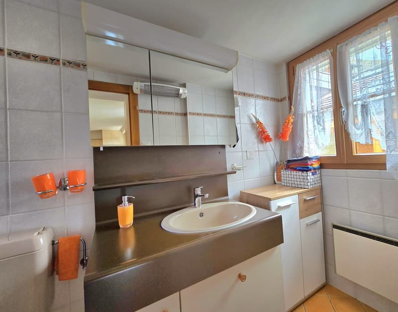 Bathroom with sink, mirror, toilet, cabinets, and a window with curtains