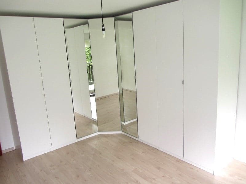 Spacious bedroom with white walls, mirrored closet doors, and laminate flooring.