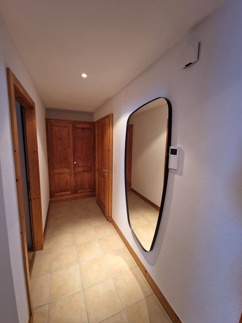 The image shows a hallway with wooden doors, a large arched mirror on the wall, and tile flooring.