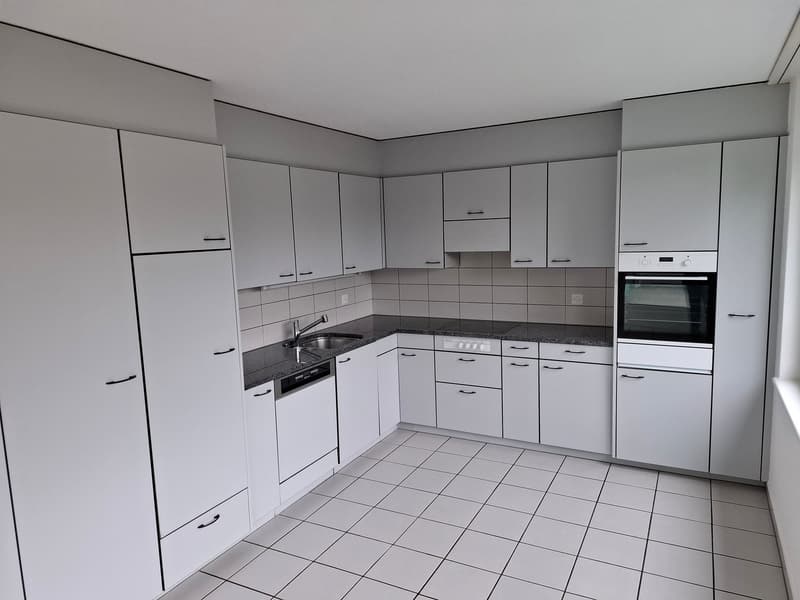 Spacious L-shaped kitchen with white cabinets, granite countertops, tiled backsplash, built-in oven, and a dishwasher