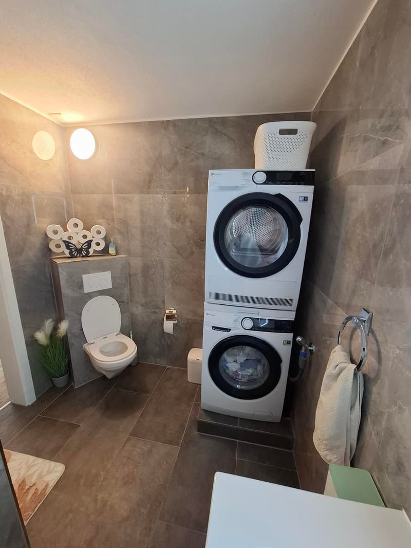 washroom with toilet, bidet, washing machine, dryer, tiled floor, marble walls, mounted lamp, towel holder