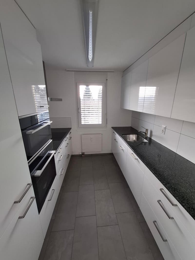 modern kitchen with white cabinets, black countertops, stainless steel sink, oven, dishwasher, and a window with blinds