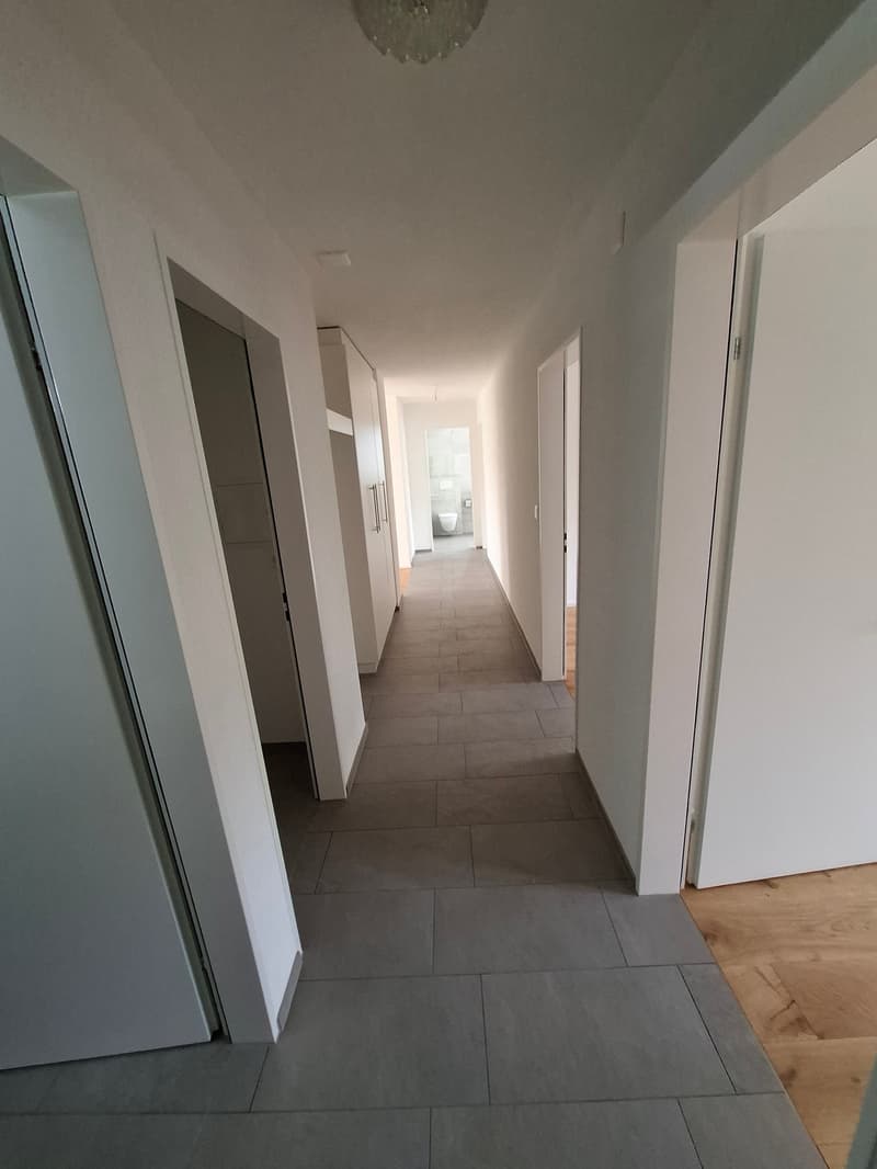 Empty hallway with tiled floor, white walls, and closed doors on both sides.