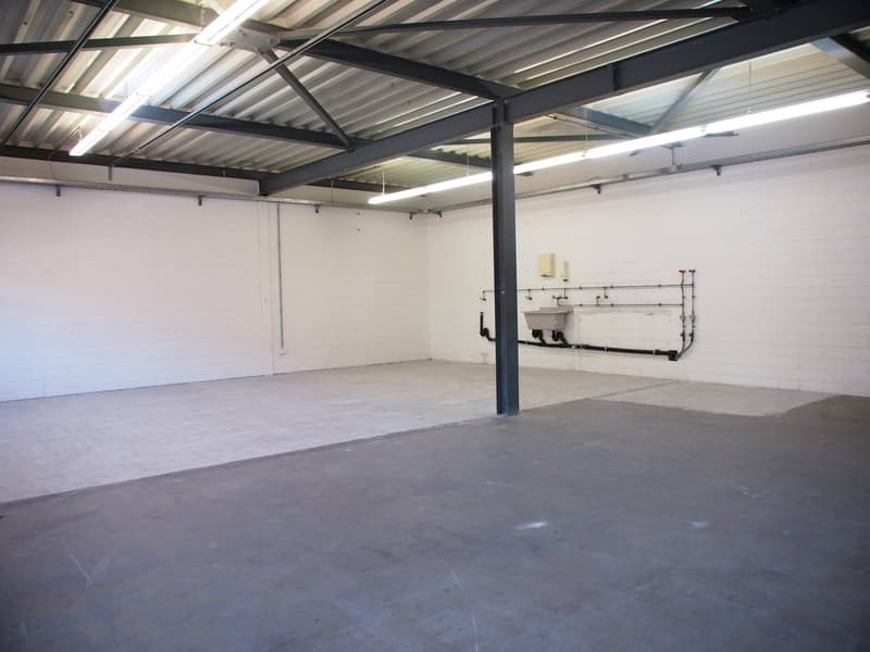 empty industrial space, concrete floor, steel trusses, white walls, fluorescent lights, metal column, sinks with pipes