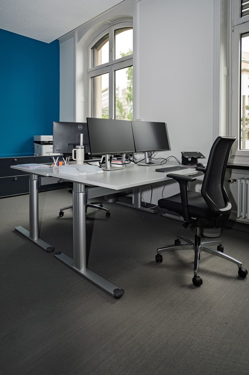 modern office setup, with a dual monitor workstation, standing desk, office chair, printer