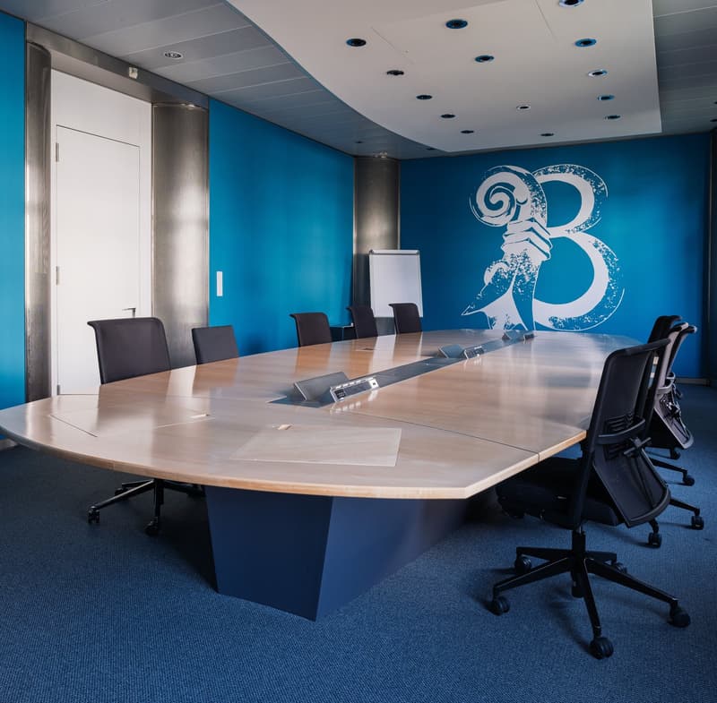 large meeting table, blue wall, metal floor, blue carpet, whiteboard, swivel chairs