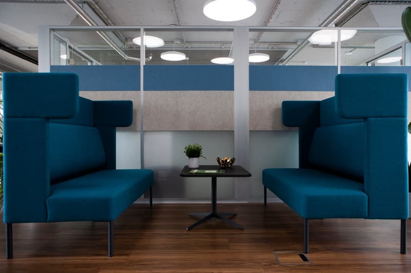 two blue modular sofas, round table, plant, silver partitions, wooden floor