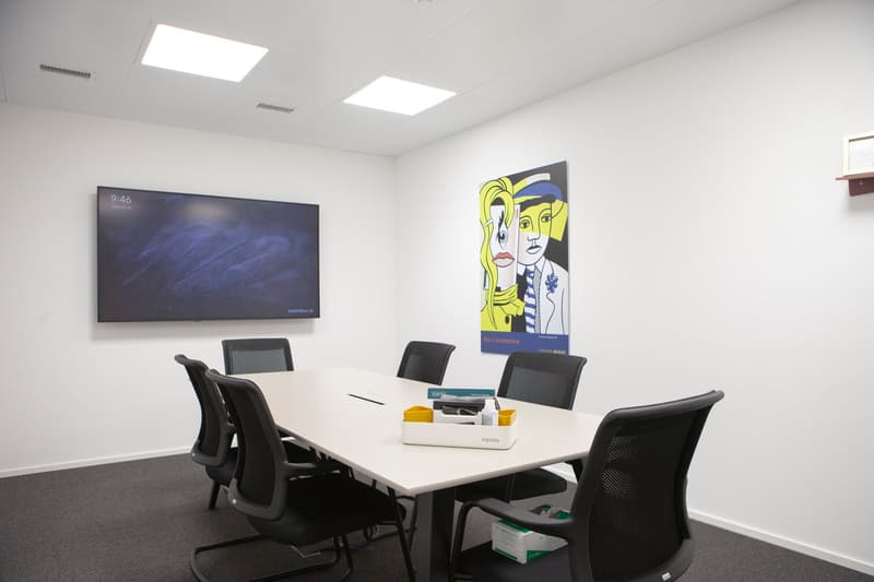 conference room with a table, black chairs, a monitor on the wall, a painting, and a box on the floor