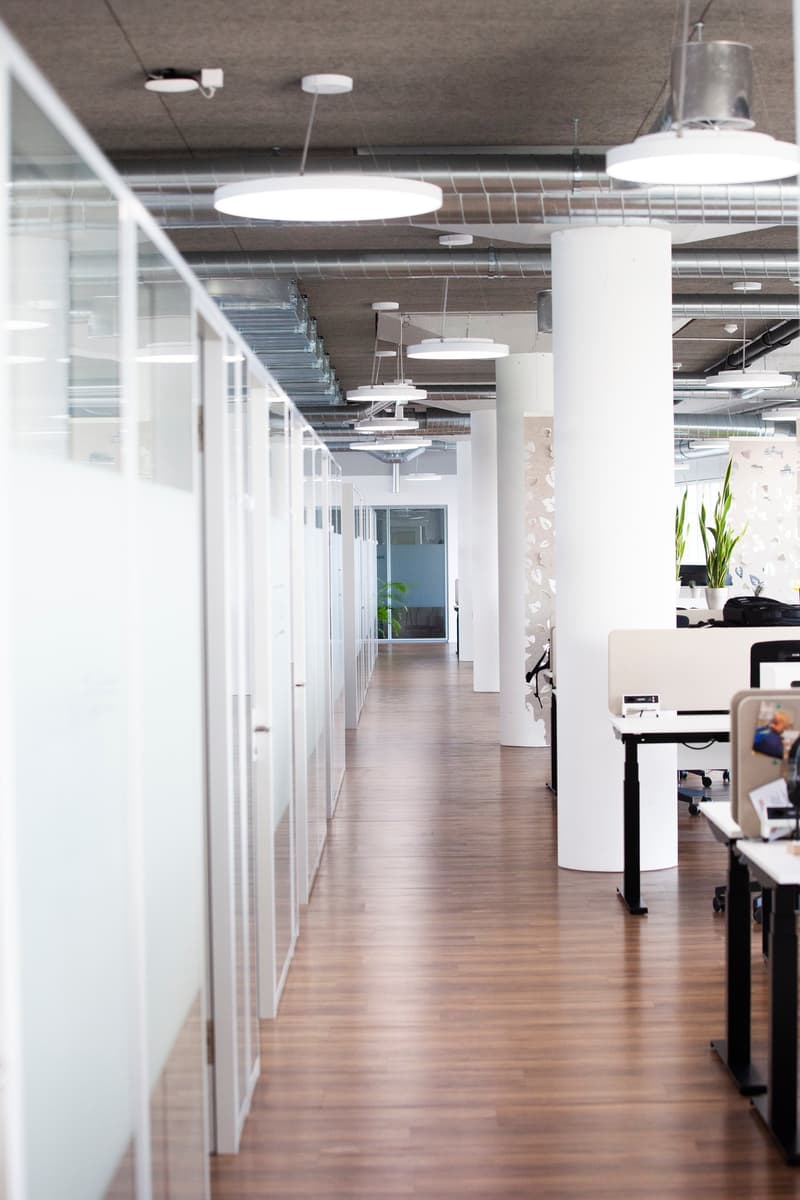 open plan office with wooden floors, glass cubicles, modern lighting fixtures, white desks, plants