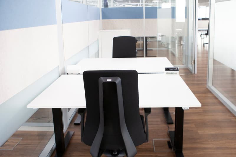 open plan office space with adjustable height desks, black chairs, and glass walls.