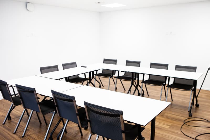 Empty conference room with a white ceiling, white walls, wooden floors, two long tables and several black chairs