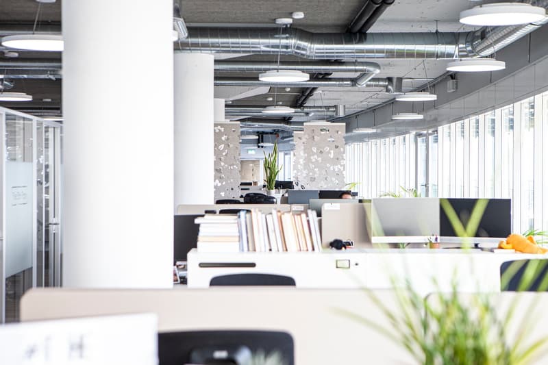 Modern office layout with large windows, contemporary desk setups, large central column, ceiling lamps