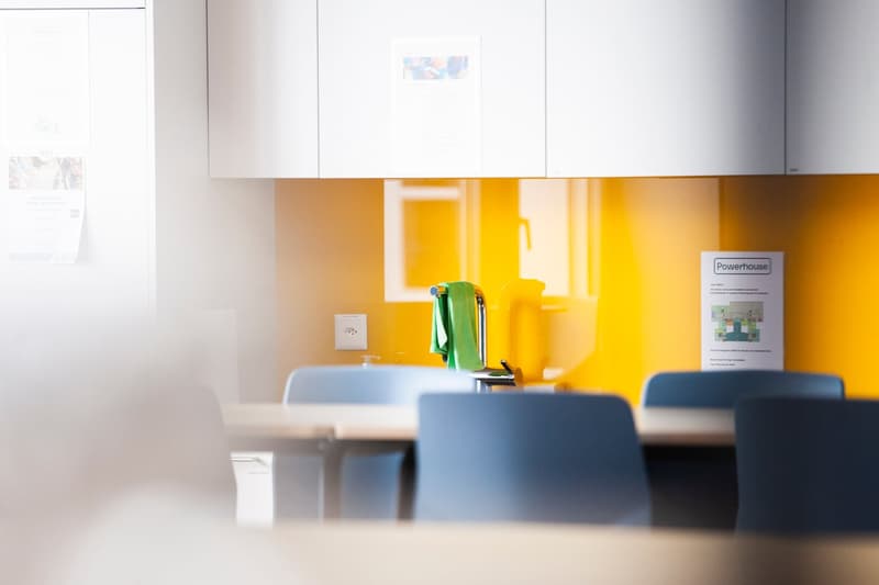 modern room, yellow wall, white cabinets, table, blue chairs, sink with faucet, yellow powerhouse sign