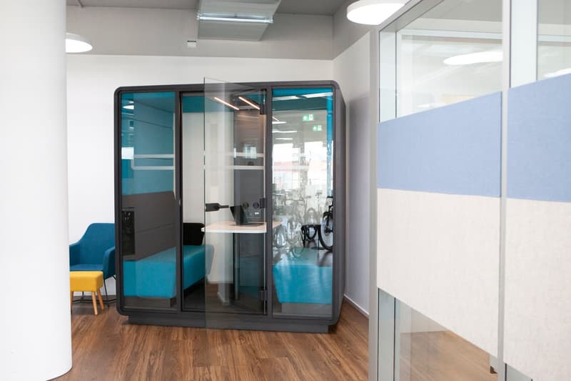 modern office room, blue and black enclosed booth, white and blue partition wall, blue chair, yellow stool, white desk, and bicycles
