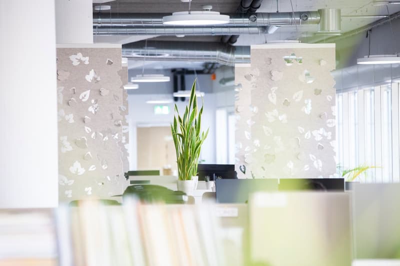 modern office space with glass partitions, greenery, monitors, desks, ceiling lights, leaf pattern screens