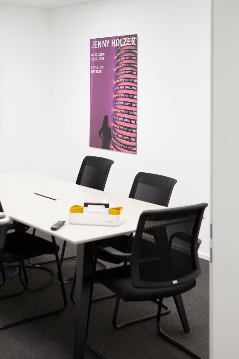 conference room, long white table, 6 black chairs, poster on wall, remote on table, pen on table