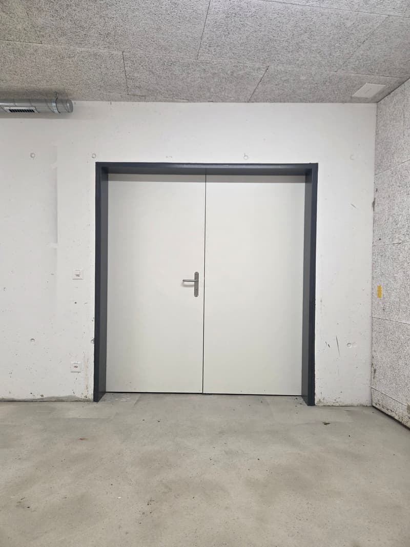 Empty room with white walls, concrete floor, double doors, and a power outlet on the wall