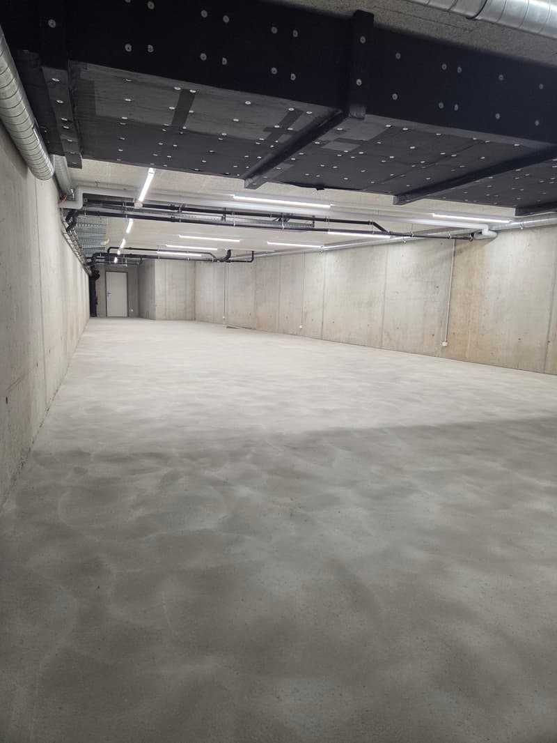 Empty concrete floor, metal beams, pipes, lights, door