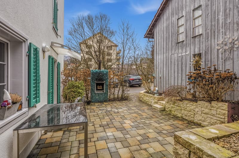 cobblestone path, outdoor glass table, green shutters, wooden wall, brick wall with plants, decorative wall art, small green fireplace, parked car