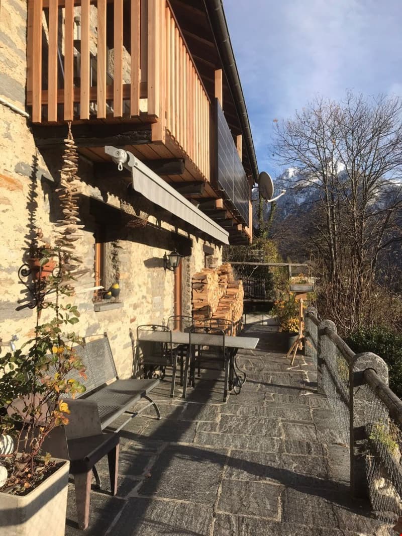 Stone building with wooden balcony, awning, outdoor seating, potted plants, panoramic view