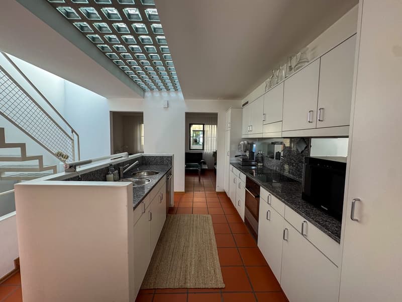Modern kitchen with granite countertops, stainless steel appliances, double sink, microwave, and tiled flooring. Kitchen has white cabinetry and white walls.