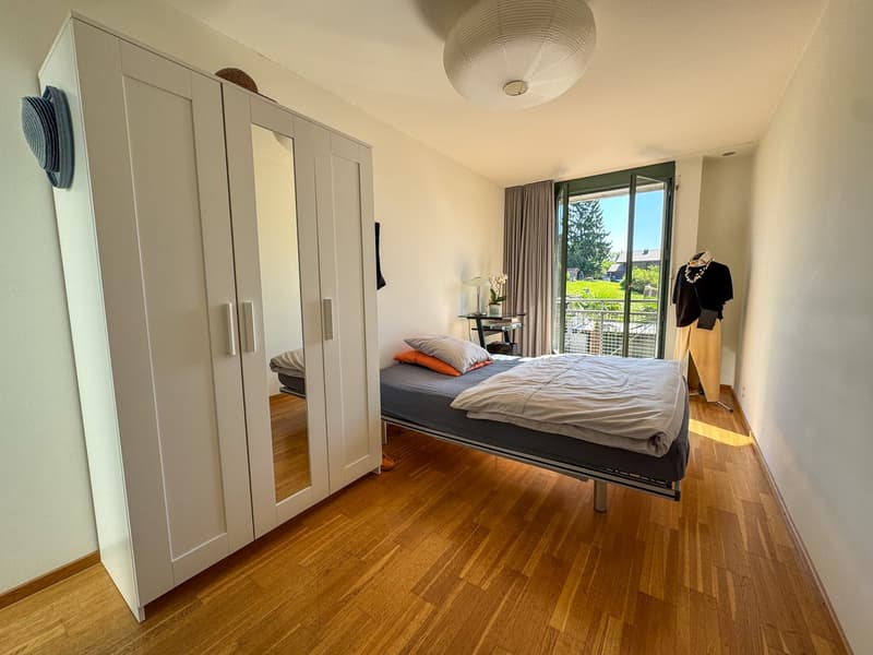Single bed, white bedding, wooden floor, wardrobe with mirror, side table with lamp, small outdoor terrace, white walls