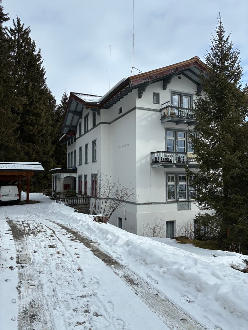 Two story building, snow covered ground, white building, wooden awning, balcony, attached garage