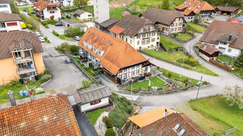 Traditional Swiss house, brown roof, white walls, multiple balconies, surrounded by other houses, located on a hill