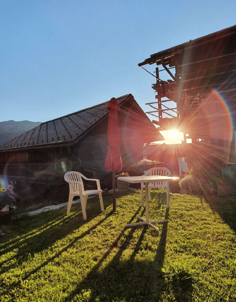 table and chairs on the lawn, wooden house in the background, sun shining through