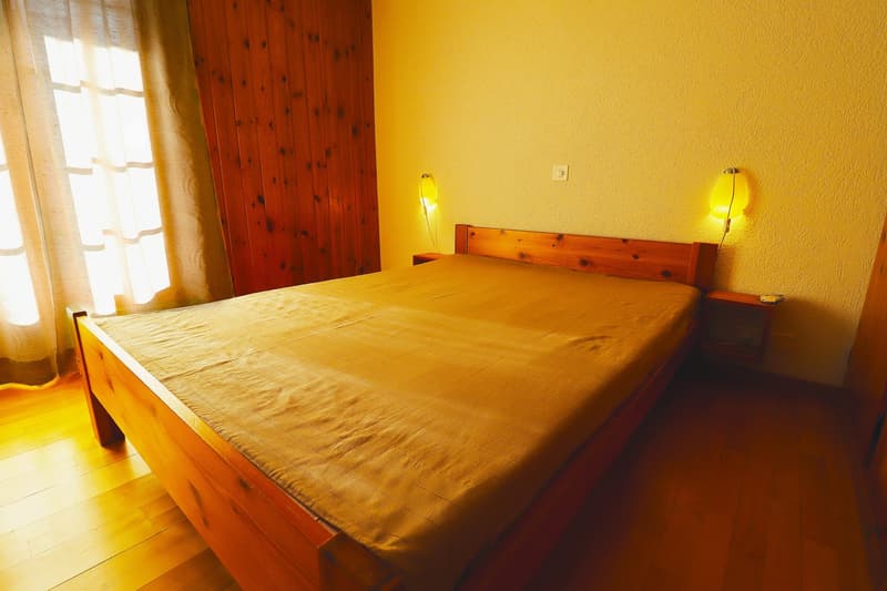 Double bed, hardwood floor, yellow walls, wooden headboard, side tables with lamps, curtains