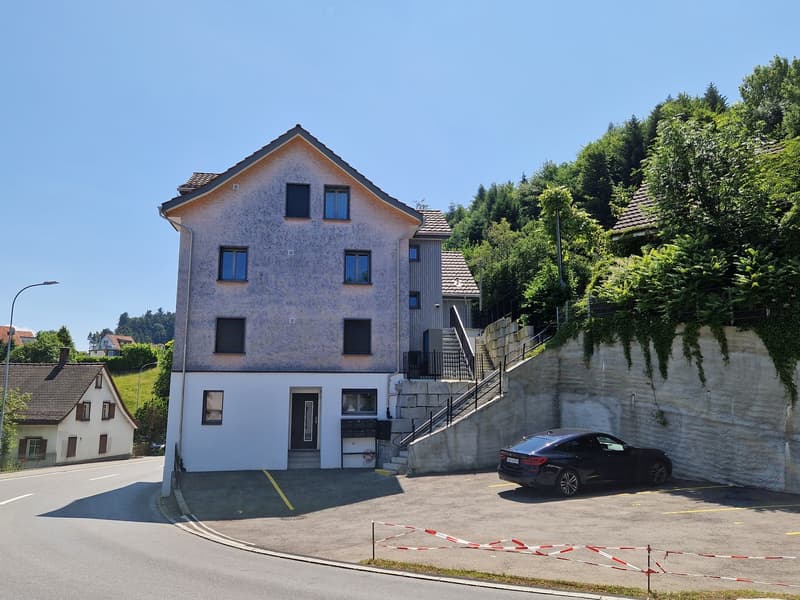 2 story house, gray exterior, white windows, black car parked in front, concrete wall, stairs leading to the entrance