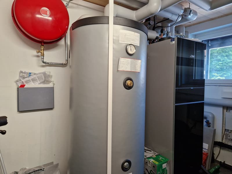 A room with a water heater, a red tank, a silver tank, a black appliance, a white pipe, a window, and a green box.