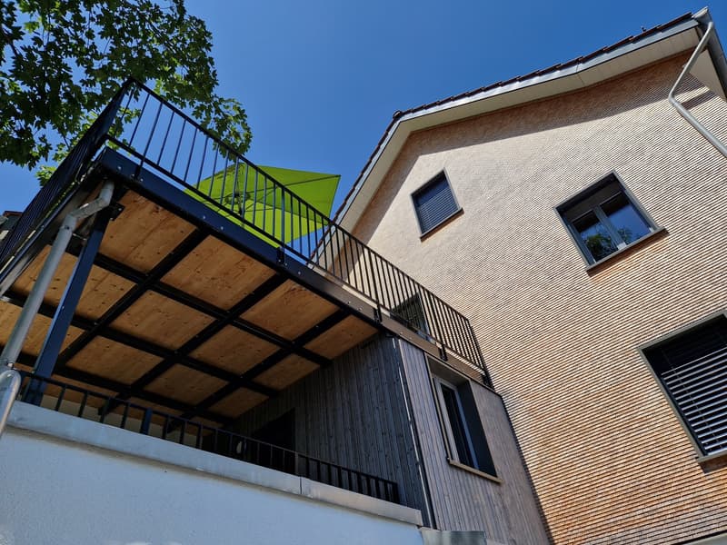 modern house, wooden balcony, metal railing, brick wall, green umbrella