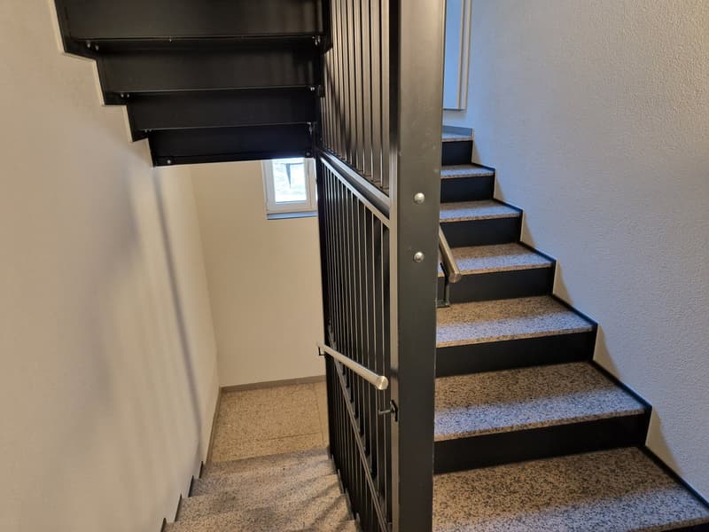 Modern staircase with black steps and handrails, granite flooring, white walls