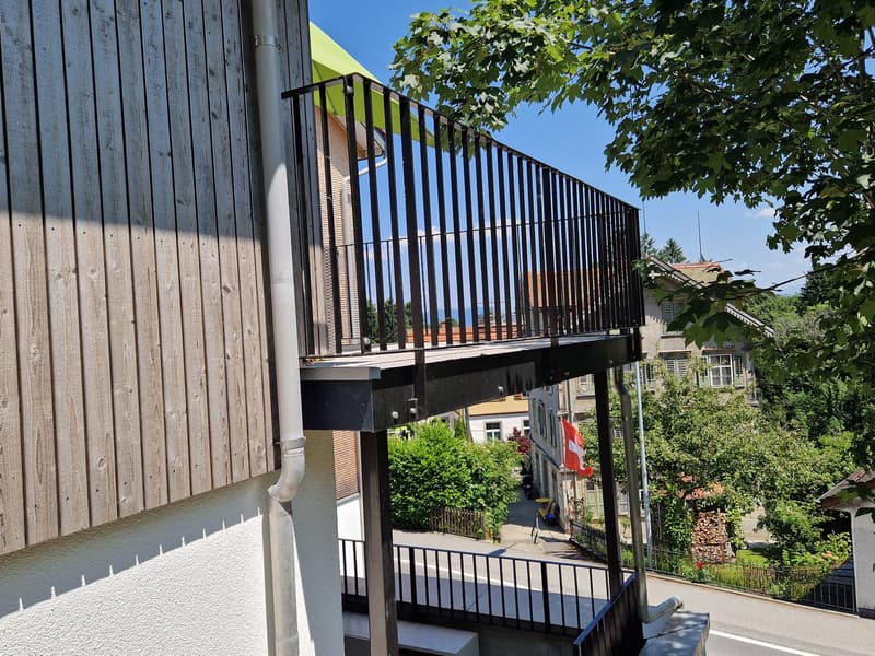 Balcony with black railings, wooden wall, green awning, street view
