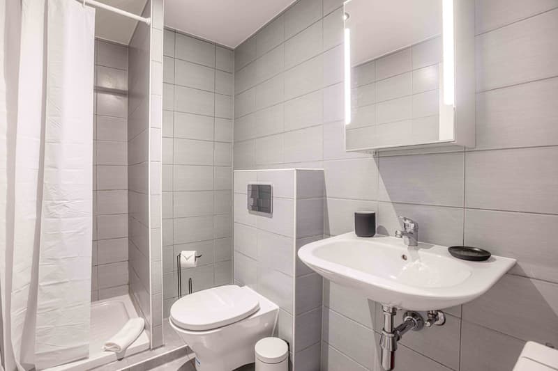 Tiled bathroom with a shower stall, toilet, and a sink with a vanity. The bathroom appears to be well-lit with recessed lighting.
