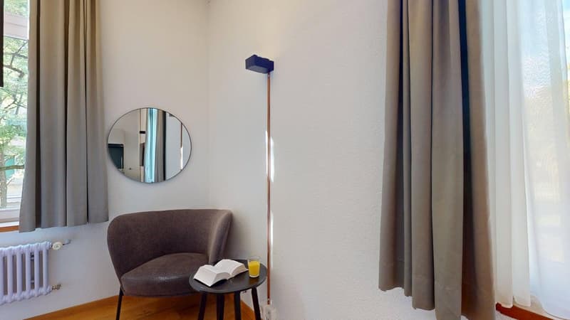 small sitting area, brown armchair, round table, mirror, radiator, white curtains