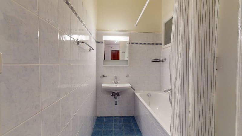 Bathroom with white tiles, blue floor, white sink, white bathtub, mirror