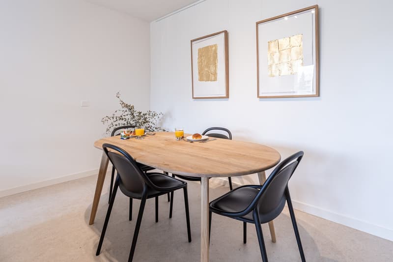modern dining room, oval wooden table, black chairs, 2 picture frames on the wall